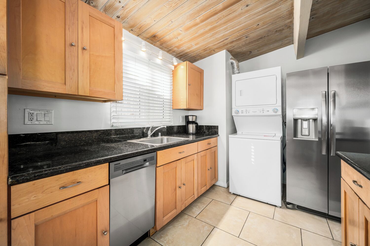 A modern kitchen with wooden cabinets, a black countertop, stainless steel appliances, and a tiled floor.