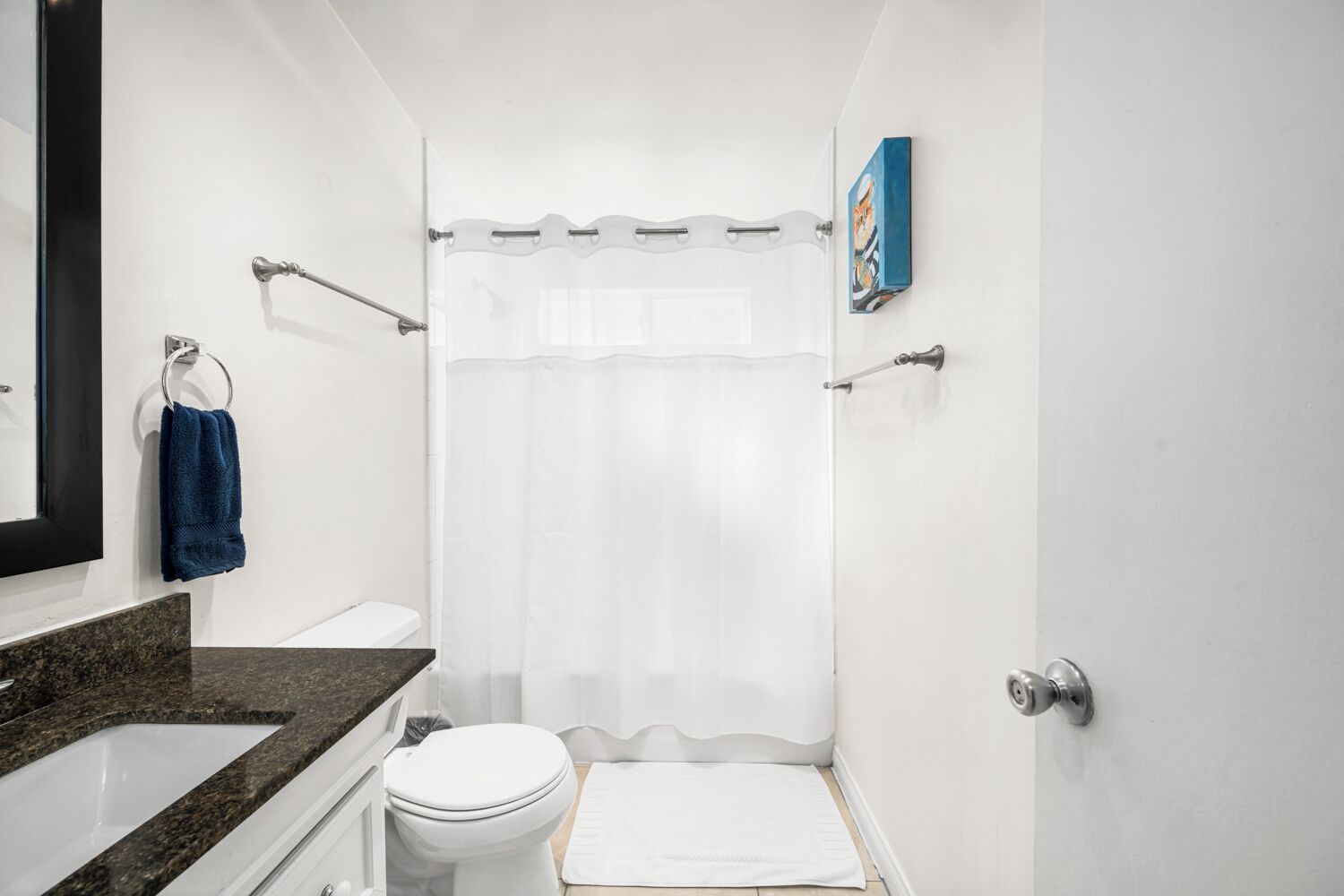 A bathroom with a white toilet, a sink with a granite countertop, a shower curtain, and a towel rack with a blue towel.