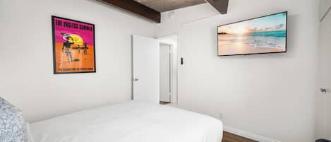 Une chambre à coucher avec un lit, une affiche, un téléviseur et une porte.
