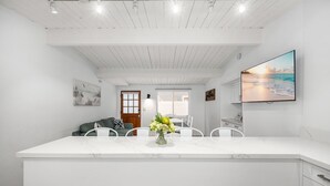 Una cocina moderna con encimera de mármol, armarios blancos y un comedor con mesa y sillas blancas.