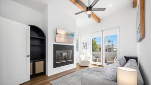 Una sala de estar moderna con chimenea, ventilador de techo y vista a través de un ventanal.