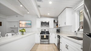 Una cocina moderna con armarios blancos, electrodomésticos de acero inoxidable y piso de baldosas.