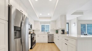 Una cocina moderna con armarios blancos, electrodomésticos de acero inoxidable y piso de madera.