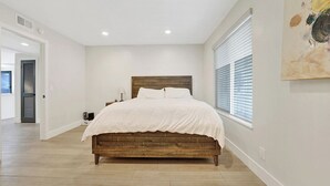 Un dormitorio con cama de madera, paredes blancas y un ventanal con persianas.