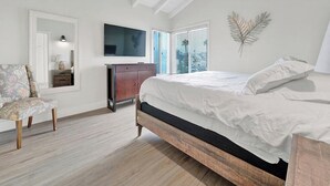 Un dormitorio con una cama de madera, una silla, un tocador, un televisor y una ventana con persianas.