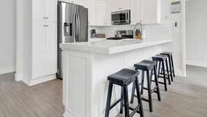 Una cocina moderna con armarios blancos, electrodomésticos de acero inoxidable y una isla central con taburetes de bar.