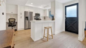 Een moderne keuken met witte kasten, roestvrijstalen apparatuur en een zwarte deur.