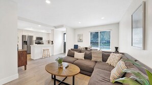 Een moderne woonkamer met een bruine bank, een ronde salontafel en een keuken op de achtergrond.
