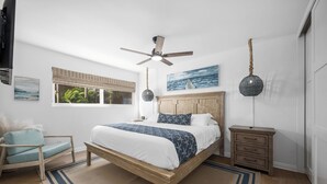 A bedroom with a wooden bed, a ceiling fan, a window with blinds, a bedside table, and a chair. - Seaside 1 BR Escape on the Iconic Newport Boardwalk (Newport Beach)