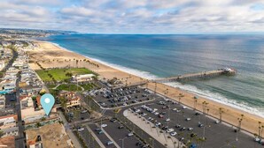An aerial view of a coastal area with a beach, a parking lot, and a pier.