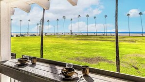 Vista desde un espacio cubierto con una mesa preparada para dos, con vista a una playa con palmeras y cielo despejado.
