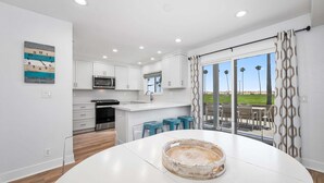 Una cocina moderna con armarios blancos, un microondas y una zona de comedor con una mesa redonda y taburetes azules.
