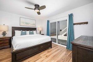 A bedroom with a bed, two bedside tables, a ceiling fan, a large window with curtains, and a view of a staircase. - **Oceanfront Oasis in Newport Beach – Steps to Balboa Park, Pier, and The Fun Zone!** (Newport Beach)