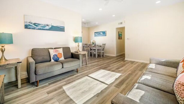 Ein Wohnzimmer mit grauem Sofa, einem Esstisch mit Stühlen und einem Deckenventilator.
