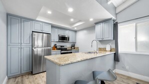 A modern kitchen with grey cabinets, stainless steel appliances, and a granite countertop. - Balboa Peninsula Hidden Gem with Private Balcony & Stunning Views (Newport Beach)