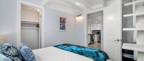 Un dormitorio con cama, armario y cocina visible a través de una puerta abierta.