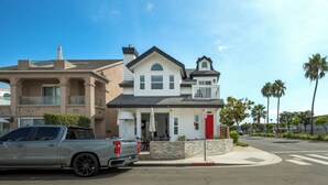 A two-story house with a red door, a balcony, and a driveway with a parked truck. - Perfect Surf Casa in Newport Near Beach and Pier (Newport Beach)