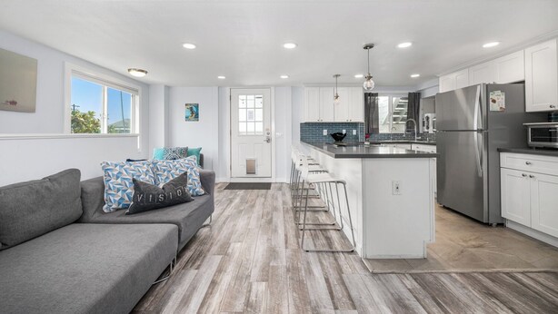 A modern kitchen with white cabinetry, a stainless steel refrigerator, and a bar area. - Perfect Surf Casa in Newport Near Beach and Pier (Newport Beach)