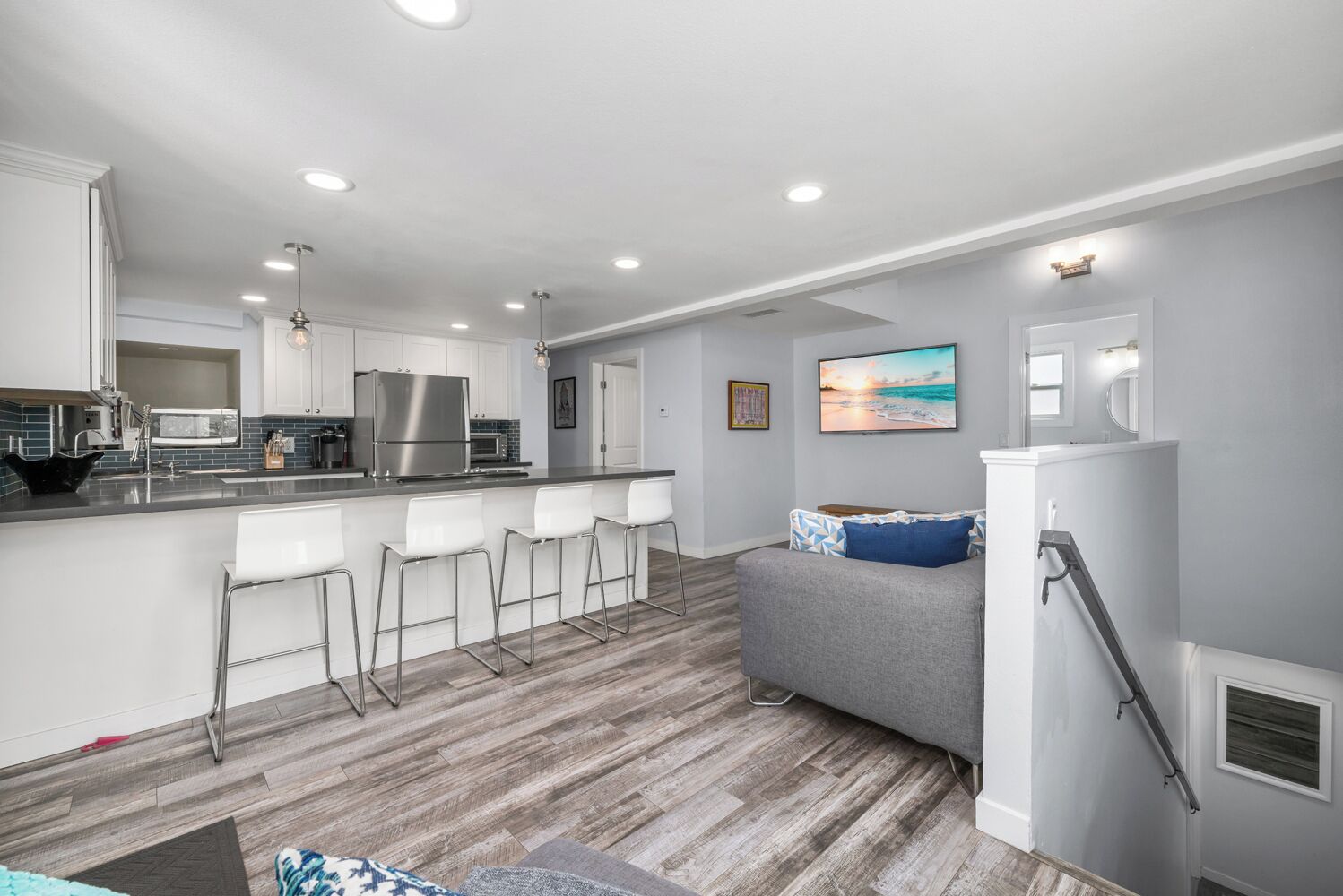 A modern kitchen with white cabinets, stainless steel appliances, and a bar area with white stools.