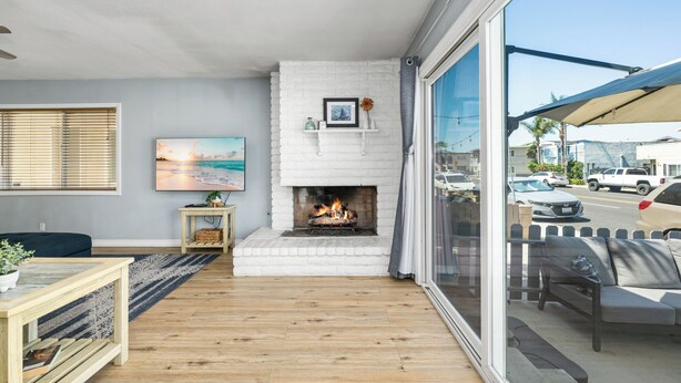 A living room with a fireplace, a large window with a view of the street, and a painting on the wall. - Balboa Hideaway w/ Patio next to Pier, Fun Zone, (Newport Beach)