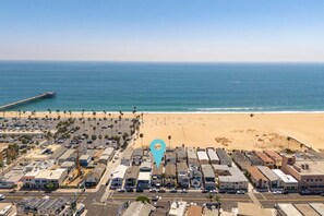 Vue aérienne d’une zone côtière avec une plage, un parking et des bâtiments.