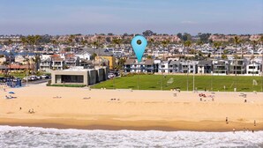 A beach with a large building, palm trees, and a view of a residential area in the background. - 2 Beachfront Condos with Private Balcony (Newport Beach)