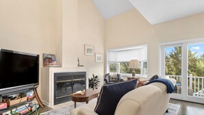 Un salon doté d’une cheminée, d’un téléviseur et offrant une vue sur l’extérieur grâce à de grandes fenêtres.