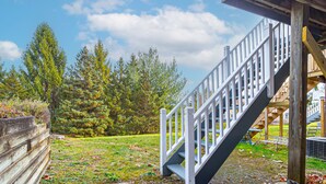Une terrasse en bois, dotée d’une rambarde blanche et d’un escalier menant à une zone abritée.