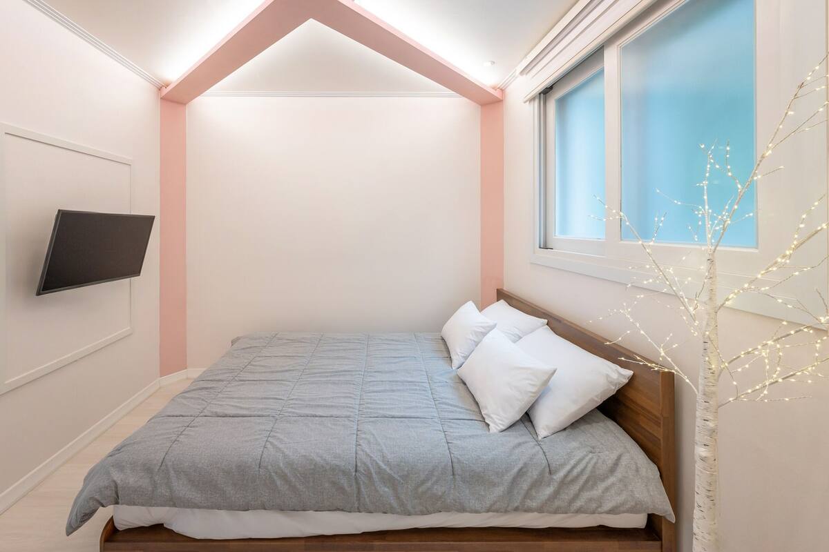 Un dormitorio con cama, televisor montado en la pared y ventana con vistas al cielo.