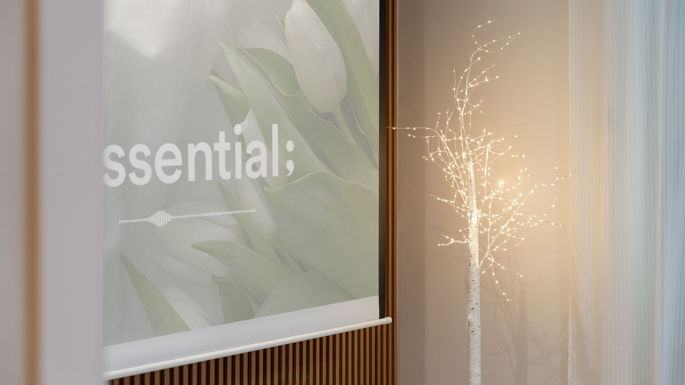 A wall with a frosted glass panel displaying the word "essential" and a decorative light installation resembling a tree.