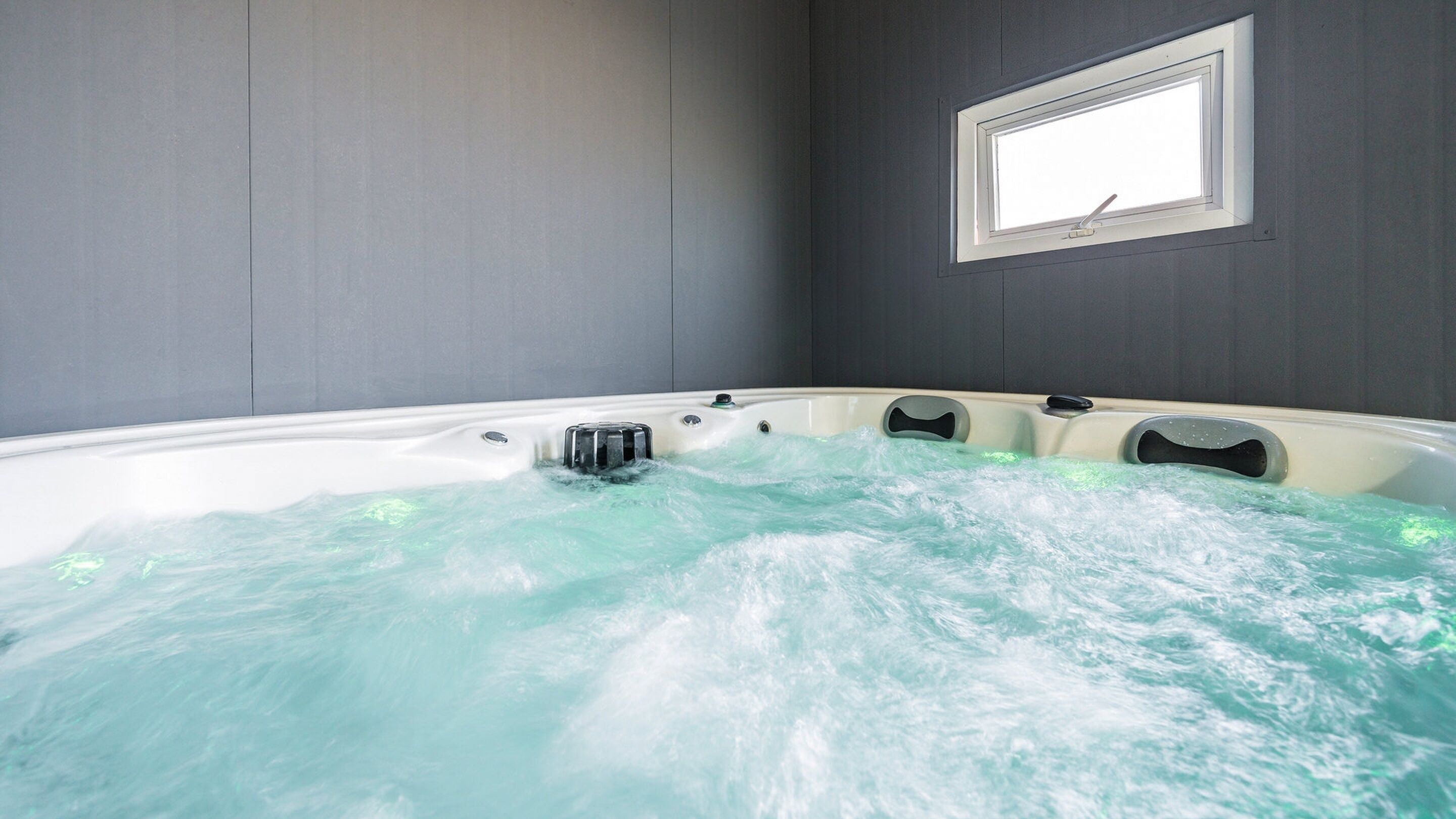 A hot tub with jets, a window, and a wall-mounted control panel.