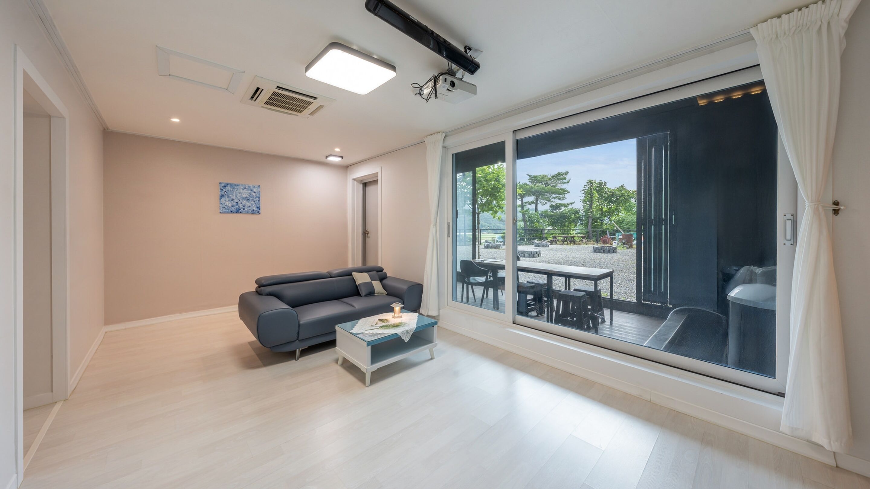A modern living room with a sofa, coffee table, and a large sliding glass door leading to an outdoor patio area.
