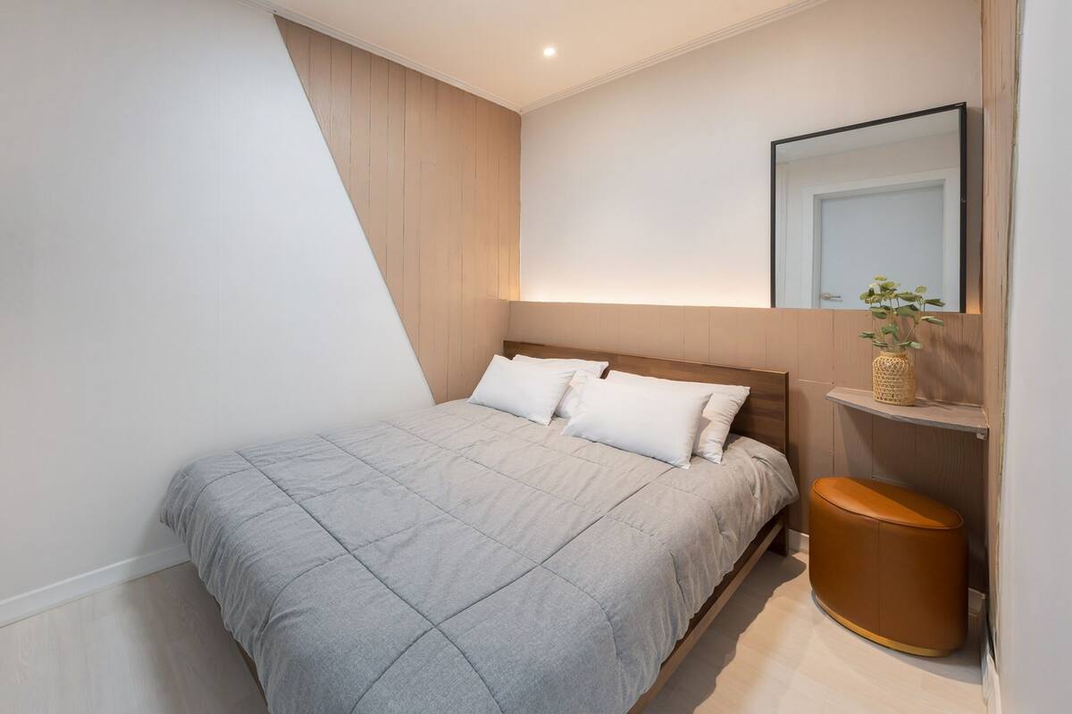 Un dormitorio moderno con cama, mesita de noche, espejo y televisor montado en la pared.