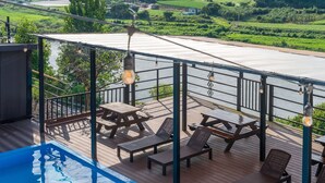 A deck with picnic tables and lounge chairs overlooking a river, with a swimming pool in the foreground. - Yeongwol You and I Spa Pension (Yeongwol)