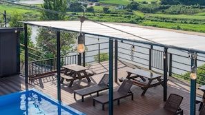 Una terraza con mesas de picnic y sillones de descanso con vistas a un río, y una piscina al frente.