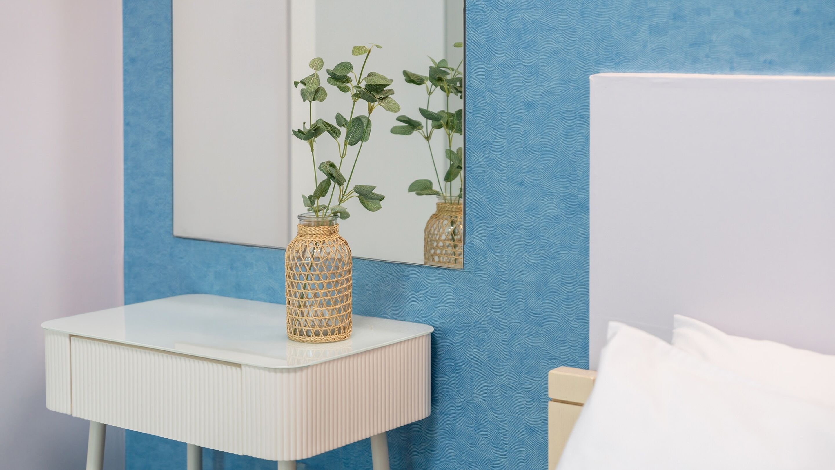 A bathroom with a white vanity, a wicker vase with green leaves, and a mirror reflecting the room.