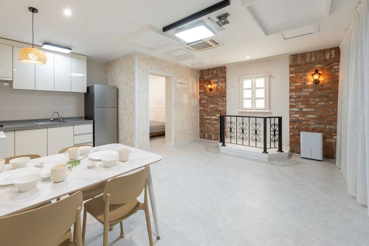 Una cocina moderna con armarios blancos, una mesa de comedor con cuencos y tazas, y una pared de ladrillo con un ventanal.