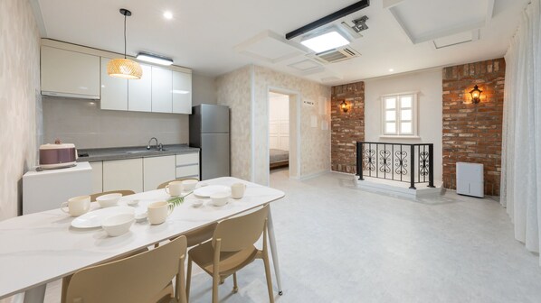 Une cuisine moderne avec des meubles blancs, une table à manger dressée avec des bols et des tasses, et un mur en briques avec une fenêtre.