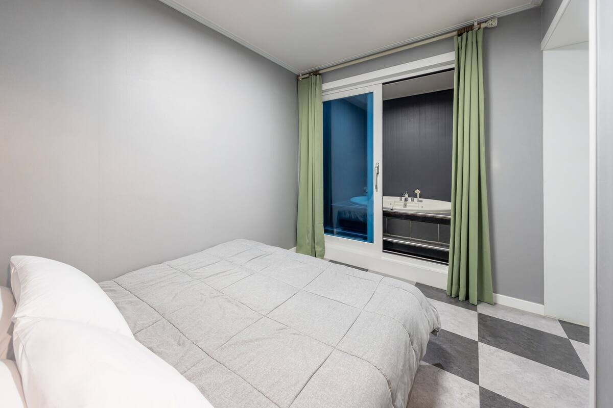 Una habitación de hotel moderna con cama, un pequeño rincón de descanso, un baño con bañera y vistas a través de un ventanal.