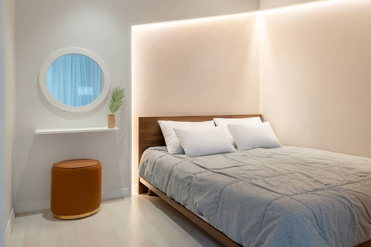 Un dormitorio moderno con una cama, un espejo redondo, una planta pequeña y un cesto de basura.