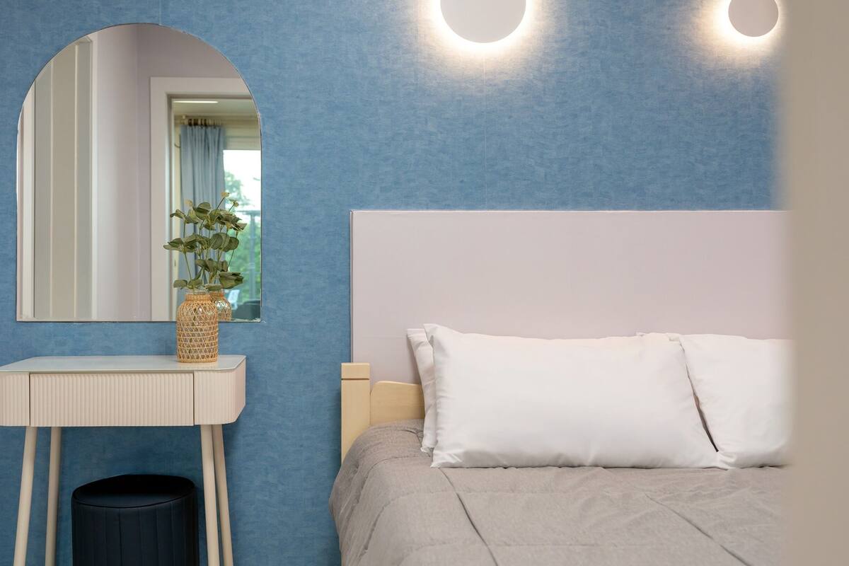 Un dormitorio con cama, una mesita de noche, un espejo y una lámpara fijada a la pared.