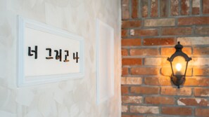 Une enseigne fixée au mur, avec des caractères coréens, un chambranle de porte blanc et un mur de briques agrémenté d’une applique murale illuminée.