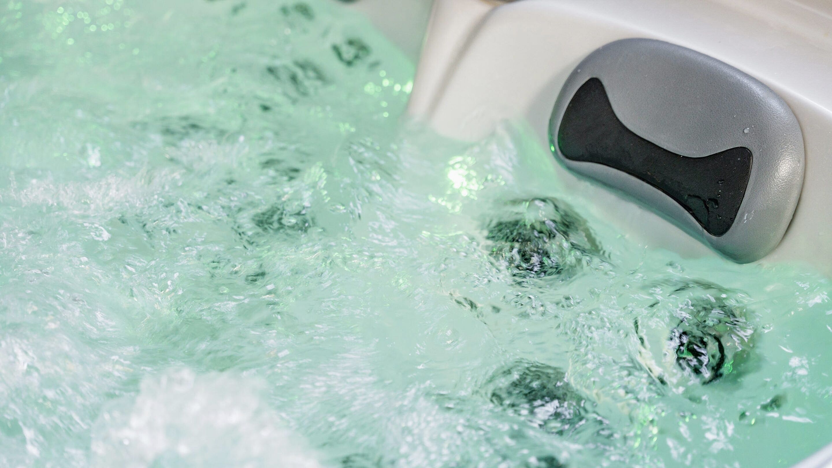 A bathtub filled with clear water and bubbles, with a black control knob on the side.