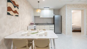 Une cuisine moderne avec des meubles blancs, un réfrigérateur en acier inoxydable et un coin repas comprenant une table et des chaises blanches.