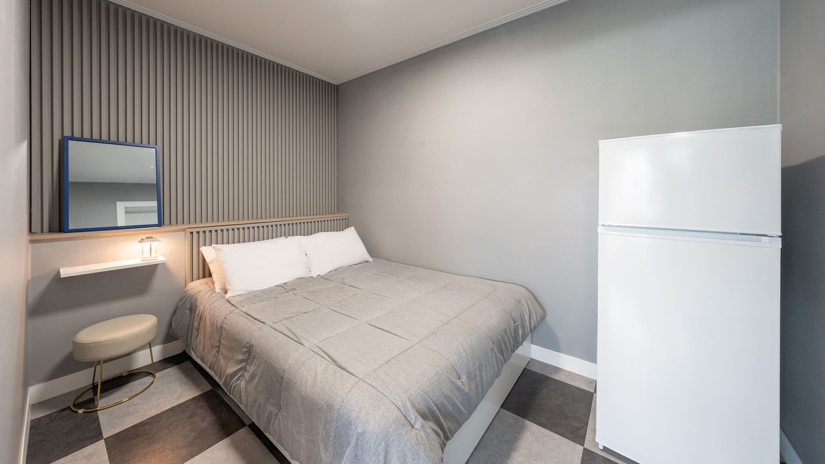 Une chambre à coucher avec un lit, une table de chevet, un miroir, un radiateur et un réfrigérateur blanc.