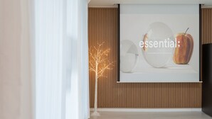 A modern interior with a projection screen displaying 'essential' and an apple, a wooden slat wall, and a decorative tree. - Yeongwol You and I Spa Pension (Yeongwol)