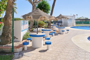 A pool area with thatched umbrellas, concrete bollards, and a clear blue sky.
