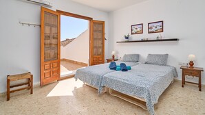 Ein Schlafzimmer mit einem Bett, zwei Nachttischen, einer Bank, einer Tür zu einem Außenbereich und zwei an der Wand befestigten Bildern.
