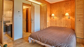 Een slaapkamer met een groot bed, houten wanden, een badkamer met een wastafel en twee wandlampen.