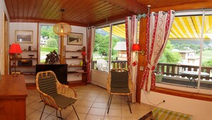 Une pièce avec un plafond en bois, deux fauteuils en osier, un bureau en bois, une télévision et une fenêtre avec des rideaux.